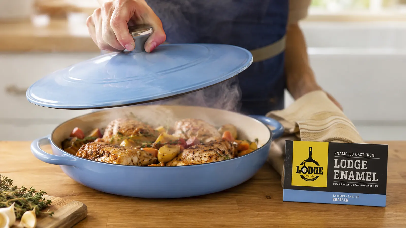 Hand lifting the lid off the enameled braiser to check on a pot of braised chicken thighs