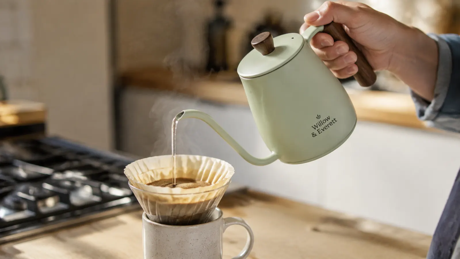 A hand tilting the gooseneck kettle to pour a thin, controlled stream of water over coffee grounds in a filter