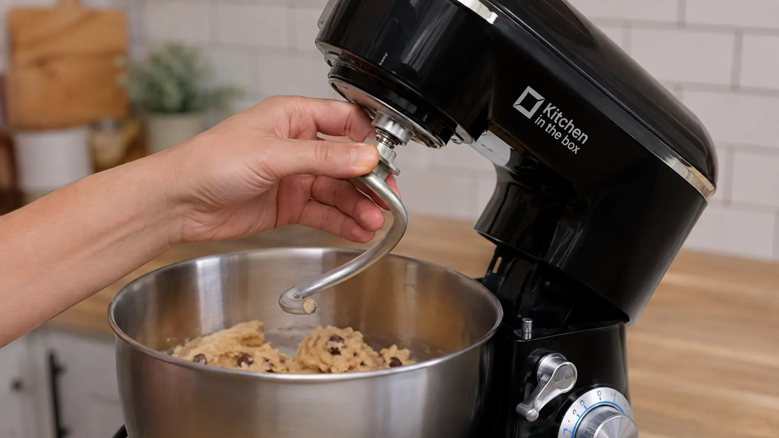Hand fitting the dough hook attachment into the head of the compact stand mixer over a bowl of cookie dough