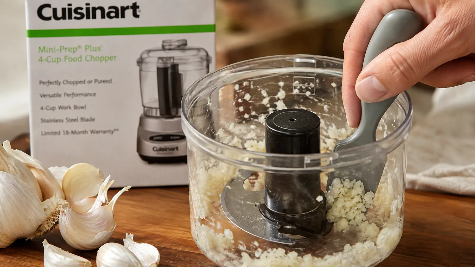 Close-up of the Cuisinart Mini-Prep Plus work bowl with minced garlic caught in the corner near the blade post, a rubber spatula scraping it out