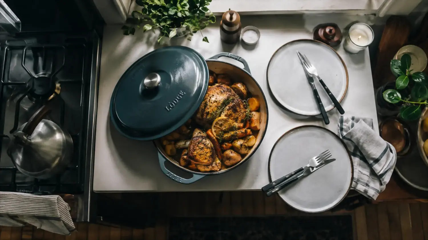 Overhead view of a shallow enameled braiser holding a finished braised chicken dinner on a narrow kitchen counter