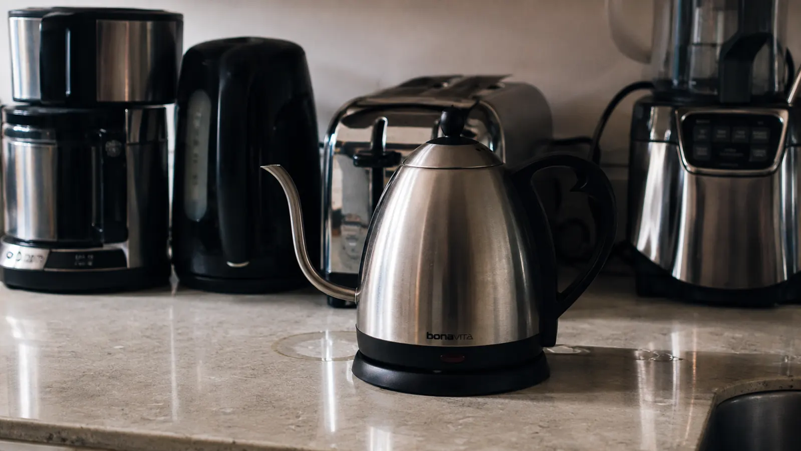 Gooseneck electric kettle sitting on a crowded small kitchen counter with a faint water ring visible on the base plate